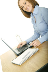 young and pretty woman in casual dress using laptop but looking at camera and smile
