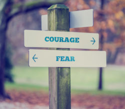 Retro style image of a rustic wooden sign in an autumn park with the words Courage - Fear offering a choice of reaction and attitude with arrows pointing in opposite directions in a conceptual image.